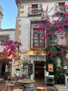 the outside of a building with tables and chairs in front of flowers growing on it