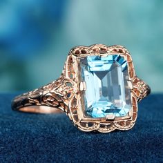 Introducing our exquisite ring, crafted in with stunning piece features a solid rose gold band, offering both elegance and durability. Adorned with a captivating Natural Blue Topaz as the primary stone, boasting an impressive 4.50 carats in a mesmerizing Emerald Cut, while the intricate filigree detailing in a floral pattern on the band adds a touch of vintage charm this ring is a timeless symbol of sophistication. This is  a truly remarkable piece. Elevate your style with this extraordinary cre Luxury Blue Topaz Ring With Filigree, Luxury Antique Topaz Ring With Intricate Design, Luxury Heirloom Topaz Ring With Intricate Design, Timeless Symbol, Topaz Color, Rose Gold Band, Filigree Ring, Natural Emerald, Gold Band