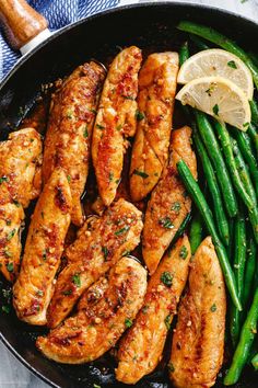 chicken and green beans in a skillet with lemon wedges