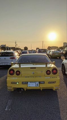 the back end of a yellow car parked in a parking lot with other cars behind it