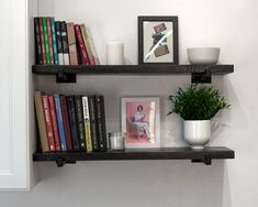 two black shelves with books, candles and pictures on them next to a potted plant