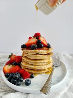 a stack of pancakes with syrup being drizzled over them and topped with berries