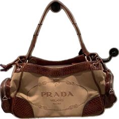 the prada handbag is brown and tan with an embellishment on it