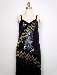 "This is a gorgeous vintage hand beaded dress fully embellished with black sequins and beads and accented with long gold glass beading in 4\" strands in an asymmetrical design. It jingles with movement ... STUNNING!! It's in excellent condition. Bust - 36/38\" Waist - 36/38\" Hips - 38/40\" Length - 34-49\" Tag Size - Large This dress comes from a pet-free and smoke-free home. If you would like more info or have any questions, please don't hesitate to ask!" Glamorous Black Sequined Flapper Dress, Gatsby Style Sequin Dress For Evening, Festive Gatsby Style Sequin Dress, Gatsby Style Sequined Dress For Costume Party, Sequin Gatsby Dress For Costume Party, Gatsby Style Embellished Sequin Cocktail Dress, Gatsby Style Embellished Sequin Dress For Night Out, Holiday Sequin Flapper Dress For Costume Party, Gold Embellished Sequin Fabric For Evening Dress