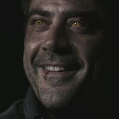 a close up of a person with yellow eyes smiling at the camera and wearing a black shirt