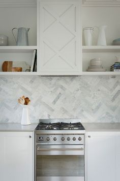 a stove top oven sitting inside of a kitchen next to white cupboards and shelves