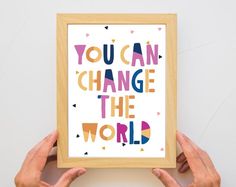 two hands holding up a framed art print with the words you can change the world