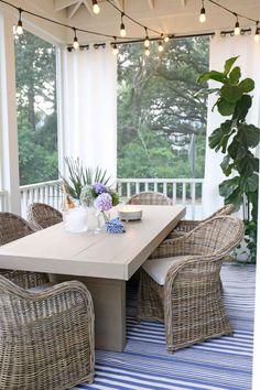 an outdoor dining area with wicker chairs and a white table on a blue striped rug