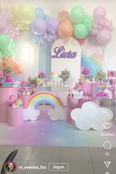 a birthday party with balloons, cake and decorations on the floor in front of a rainbow arch