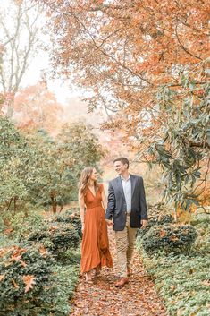 an engaged couple holding hands and walking down a path in the woods during their fall engagement session