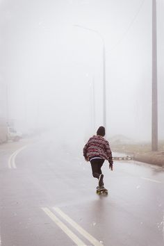 a person riding a skateboard down a street in the middle of foggy weather