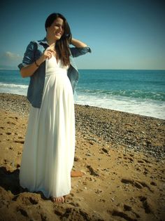 a woman standing on top of a sandy beach next to the ocean wearing a white dress