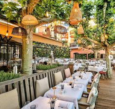 an outdoor dining area with tables, chairs and umbrellas hanging from the trees above