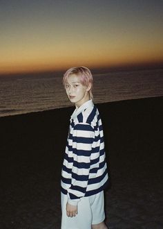 a young man standing on top of a sandy beach next to the ocean at sunset