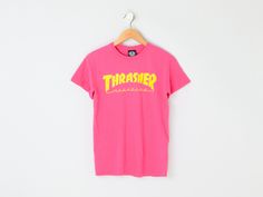 This vintage 2000s t-shirt has sharp graphics. The tag size is S - it measures 18" across the chest laid flat, and it measures 26" long shoulder-to-hem. This item is in excellent vintage condition.   Tag information:  - 100% cotton - Machine wash cold. Tumble dry low. - Originally by Thrasher Size and fit:  - Tag size is S   - Chest: 18" across    - Length: 26" long shoulder-to-hem Pink Y2k T-shirt For Streetwear, 90s Style Pink T-shirt With Letter Print, Pink Urban T-shirt For Streetwear, 90s Letter Print T-shirt For Skateboarding, 90s Skateboarding Letter Print T-shirt, Pink Graffiti Print T-shirt For Streetwear, Retro Pink T-shirt For Streetwear, 90s Style Pink T-shirt With Graphic Print, 90s Pink T-shirt For Streetwear