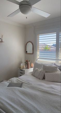 a bedroom with a white bed and ceiling fan in the corner next to a window