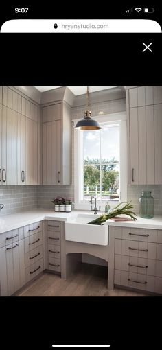 an image of a kitchen with white cabinets and wood flooring in the background, there is a large window above the sink