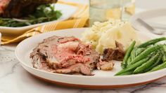 a plate with meat, mashed potatoes and green beans on it next to a glass of water