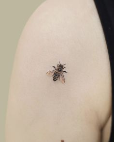 a small bee tattoo on the back of a woman's left shoulder and upper arm