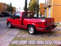 a red pick up truck parked on the side of a road next to a building