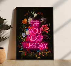 a neon sign that says see you next tuesday with flowers in the background and a potted plant