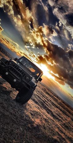 a truck is parked in the middle of a field at sunset with clouds above it