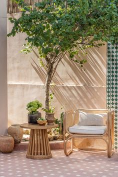 a chair and table sitting under a tree near a wall with potted plants on it