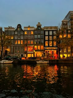 several boats are parked on the water in front of some buildings and trees at night