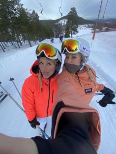 two people on skis taking a selfie with snow goers in the background