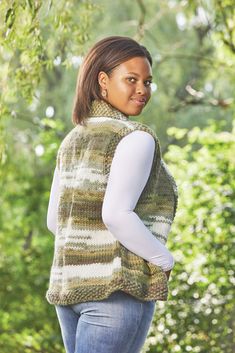 a woman standing in front of some trees wearing a sweater and leggings with her hands on her hips