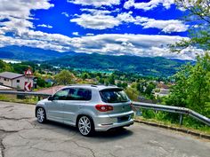 a silver car parked on the side of a road next to a forest and mountains