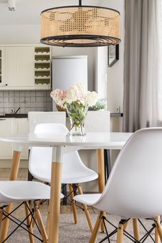 a white dining room table with chairs and a vase filled with flowers on top of it