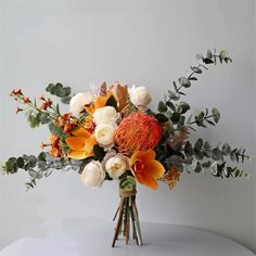 an arrangement of flowers and greenery in a vase on top of a white table