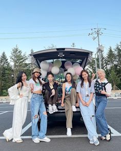 four girls standing in front of a car with balloons on the back and one girl holding her hand up