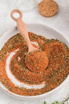 a wooden spoon in a white bowl filled with seasoning next to two other spices