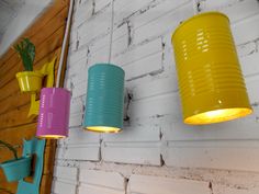 three yellow and blue tin can lights hanging on a brick wall next to a potted plant