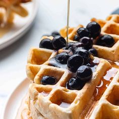 a stack of waffles with syrup and blueberries on top sitting on a plate