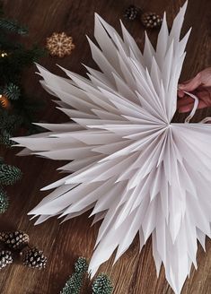 a person holding a white paper ball on top of a wooden table next to christmas decorations