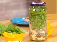 a jar filled with green vegetables sitting on top of a wooden table next to lemons