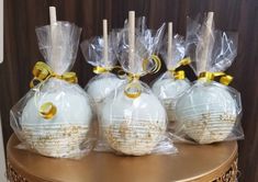 four white balls wrapped in plastic and tied with gold ribbon on a table next to candles