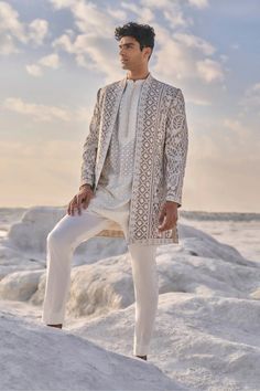 a man standing on top of a rock next to the ocean wearing a white suit