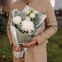 a man holding a bouquet of white flowers in his hands and wearing a brown coat