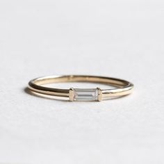 a gold ring with a baguette cut diamond in the middle, on a white surface