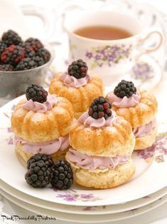 small pastries on a plate with blackberries and raspberries next to a cup of tea