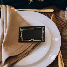 a place setting with napkins, goldware and an empty black sign on the plate