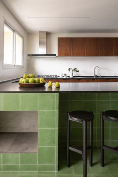 a kitchen with green tile counter tops and stools in front of an island that has fruit on it