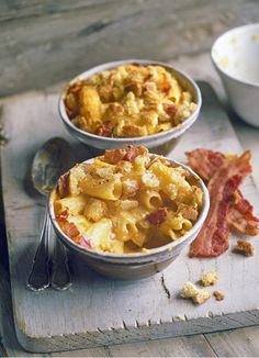 two bowls filled with macaroni and cheese on top of a cutting board