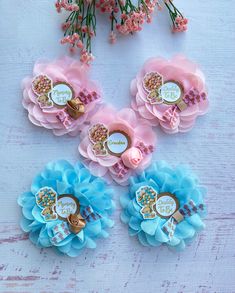 four pink, blue and gold flower hair clips on a white table with flowers in the background