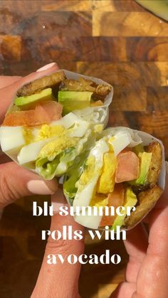 someone holding up a half eaten sandwich with lettuce and tomato on it, in front of a wooden table