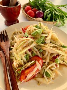 a white plate topped with pasta and veggies next to a bowl of tomatoes